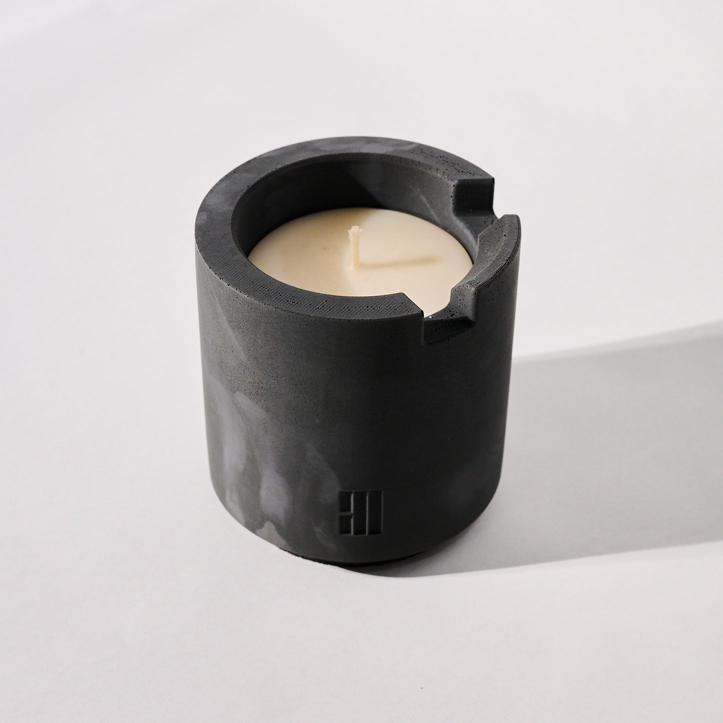 Concrete Crenel candle vessel with a white candle inside on a white background
