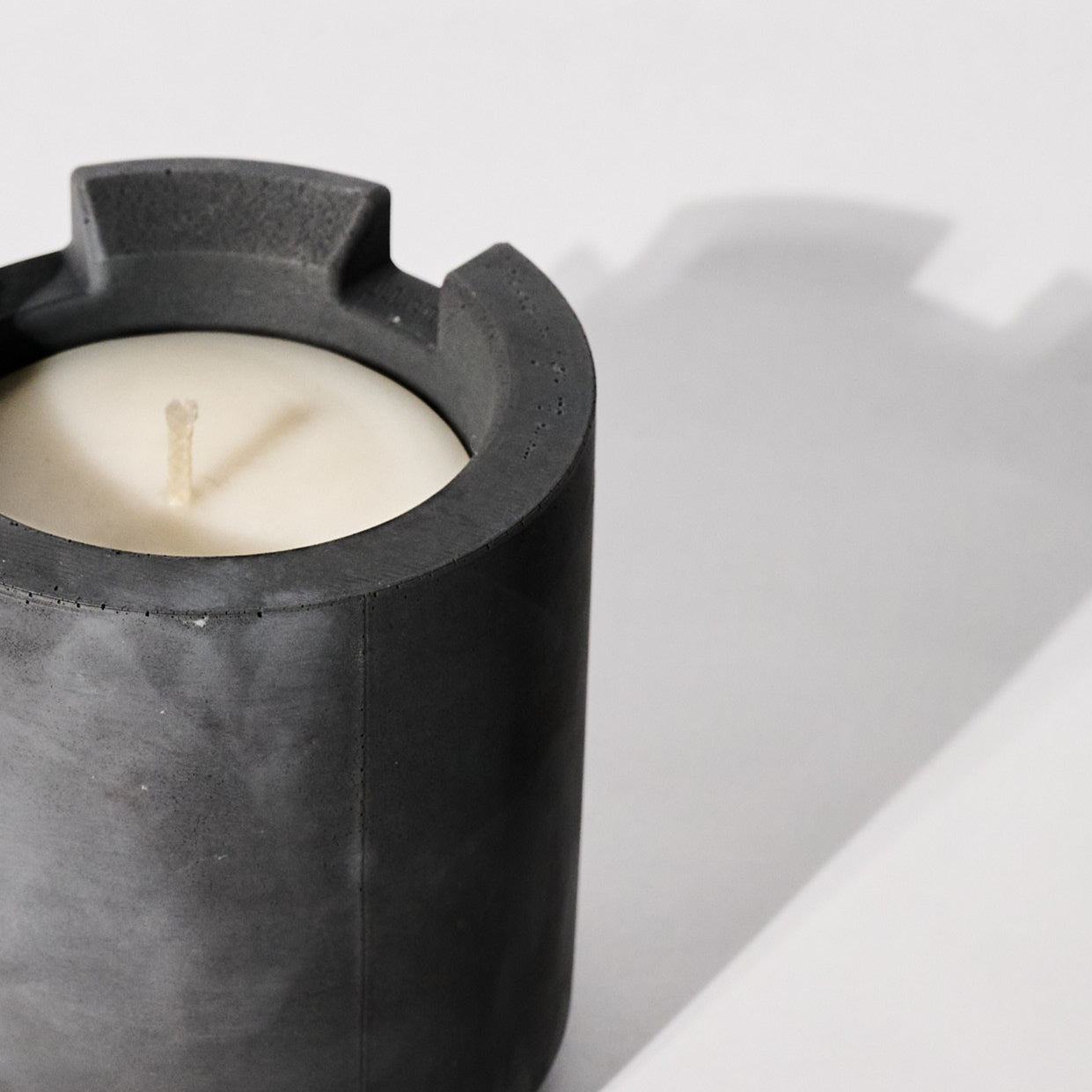 Candle in a dark gray concrete vessel on a light white