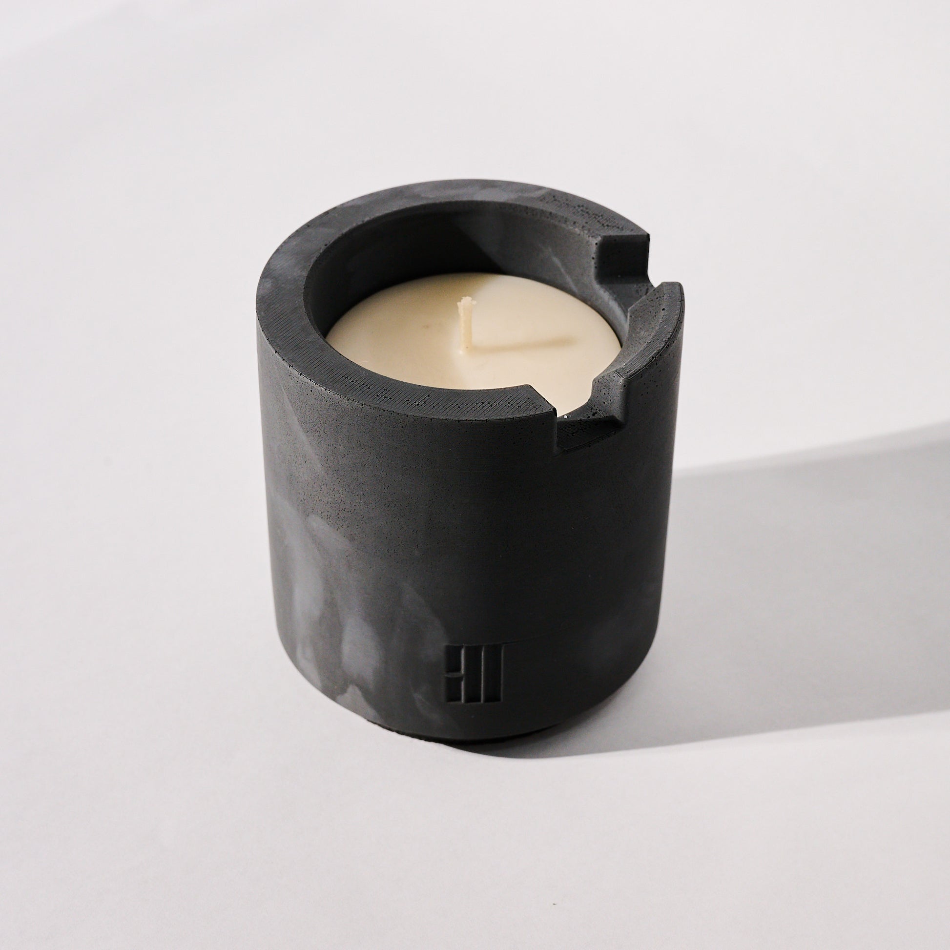 Concrete Crenel candle vessel with a white candle inside on a white background