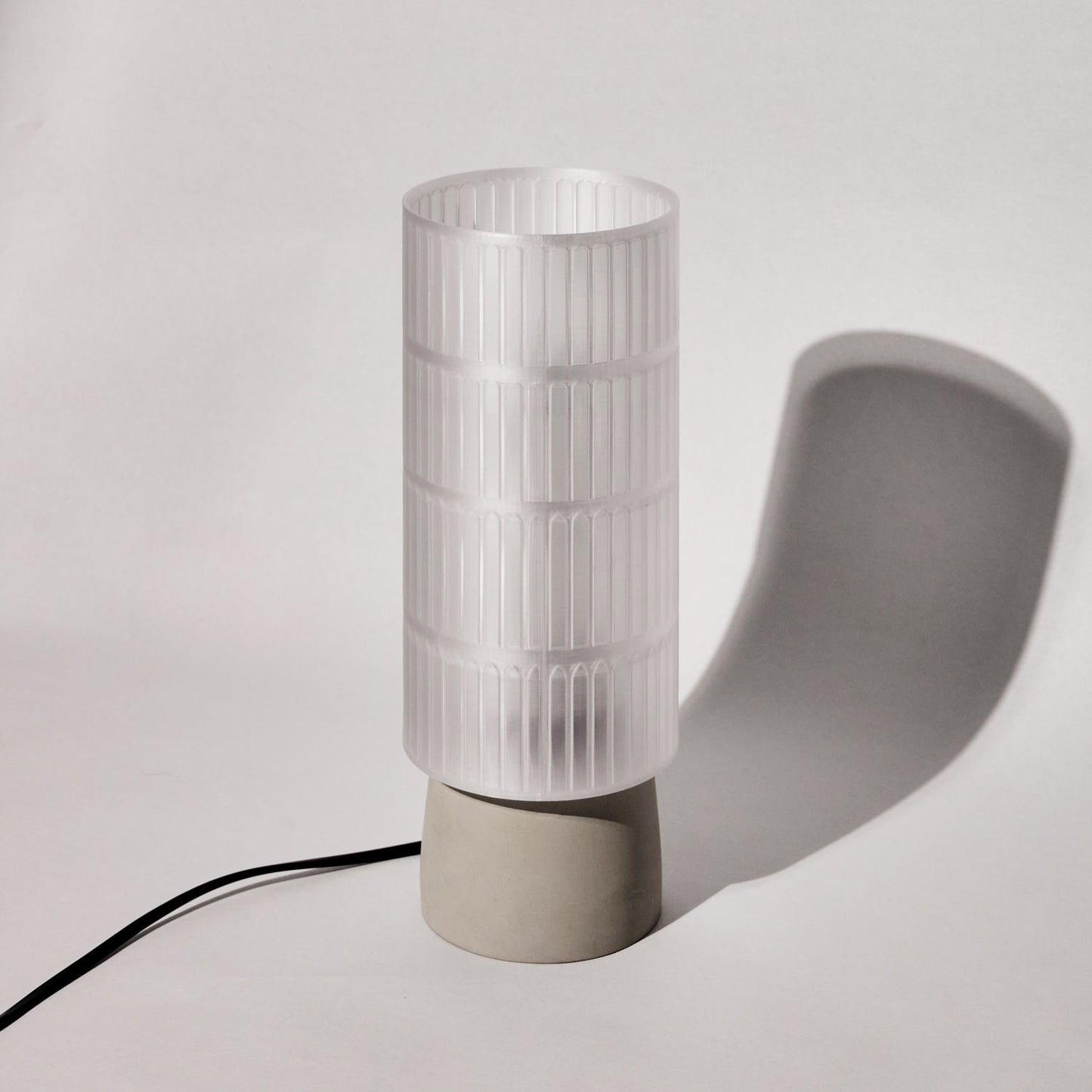 Table lamp with a cylindrical white glass shade and beige base on a light gray background
