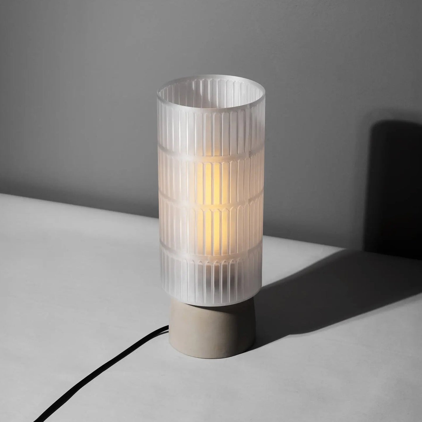 Table lamp with ribbed 3d printed shade on a gray surface against a dark gray wall