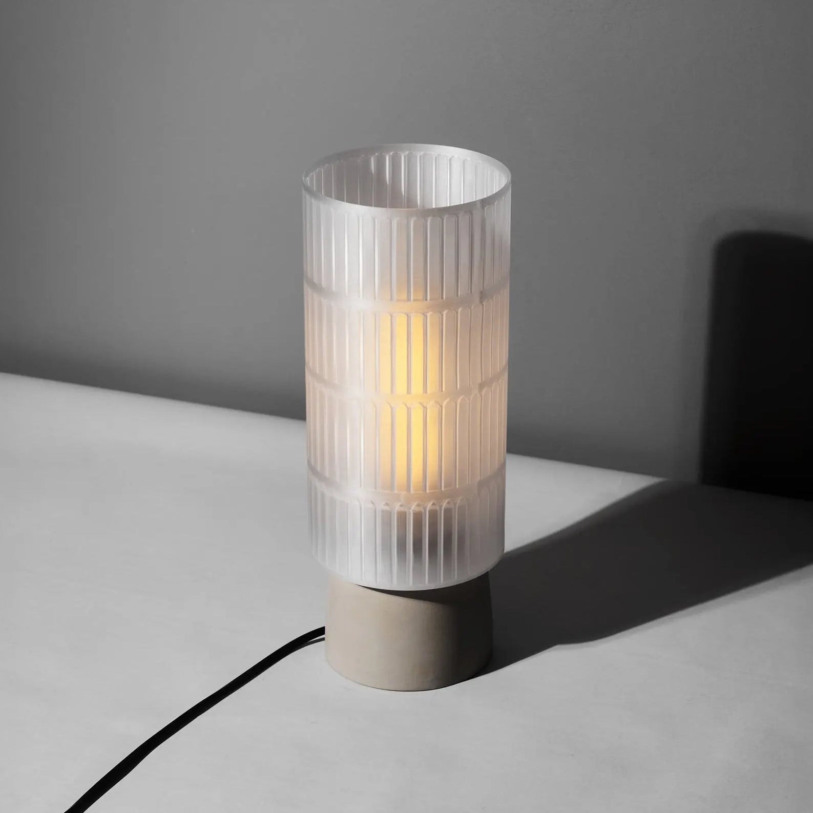 Table lamp with ribbed 3d printed shade on a gray surface against a dark gray wall
