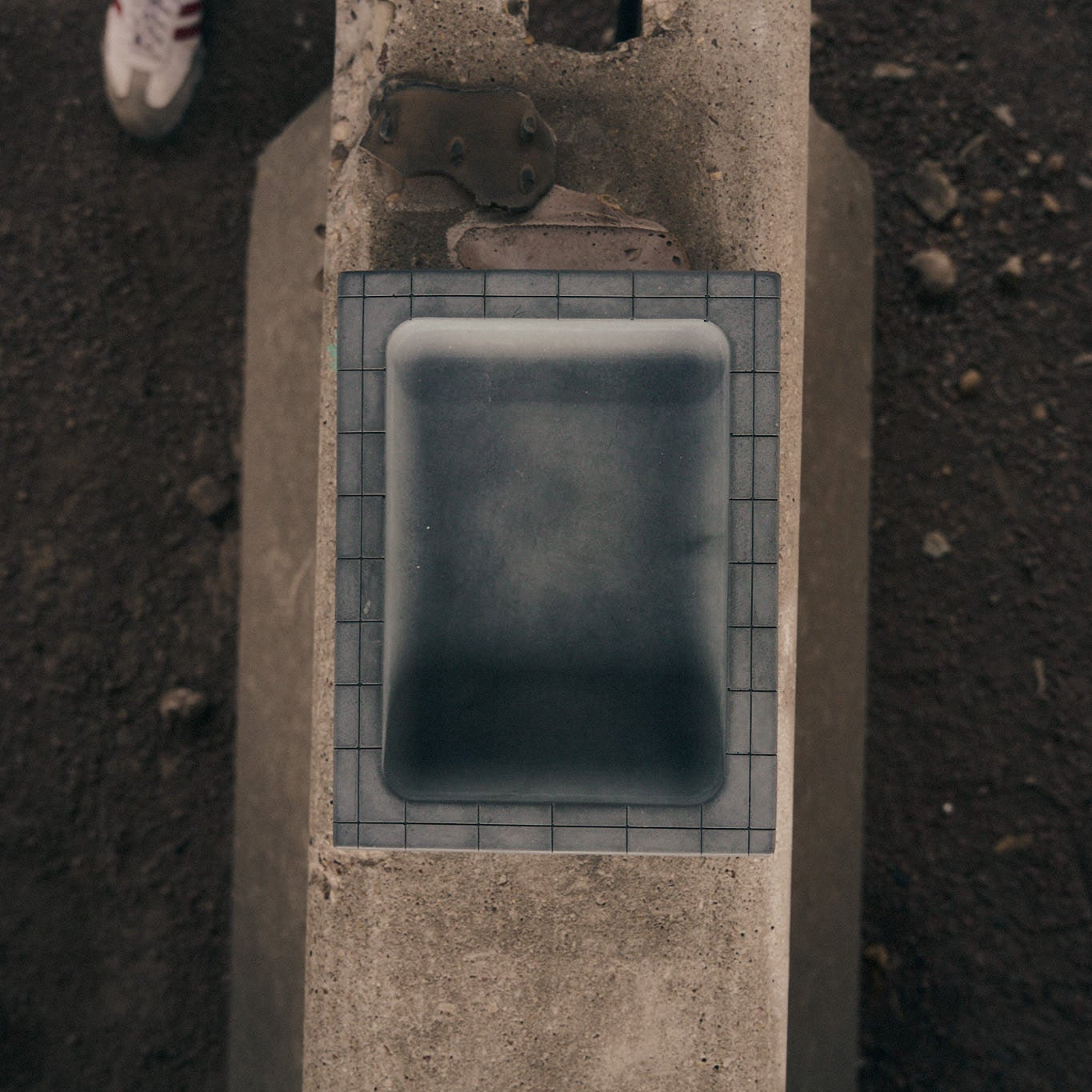 Illfound gray concrete entryway tray sitting on concrete ballard.